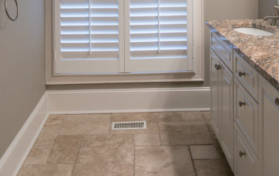 A room with a limestone tile floor, white wooden shutters on the window, and a granite countertop with a sink.
