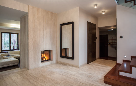 A room with a clean travertine floor and a lit fireplace.