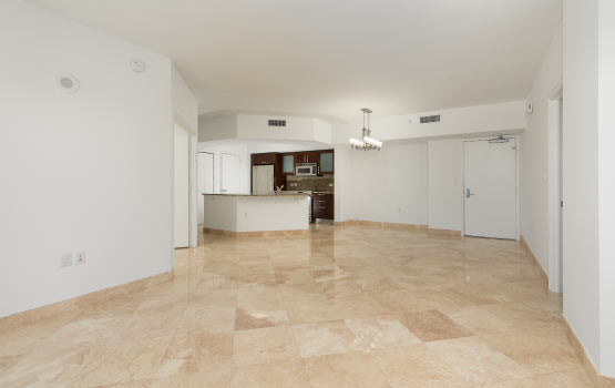 Spacious room with a polished travertine floor and modern kitchen in the background.